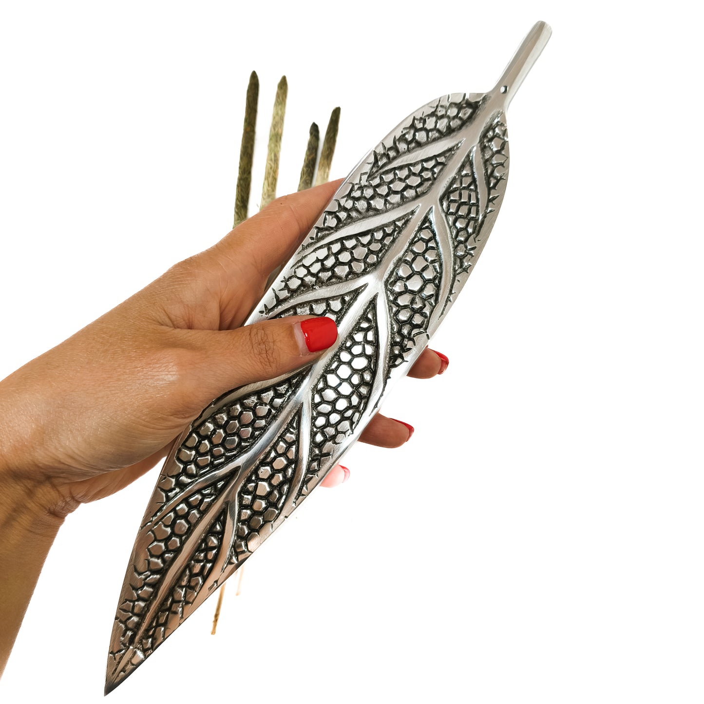 Un porta incienso de metal con forma de hoja, diseñado para sostener una varilla y recoger la ceniza. La varilla de incienso está encendida y el humo se eleva suavemente.